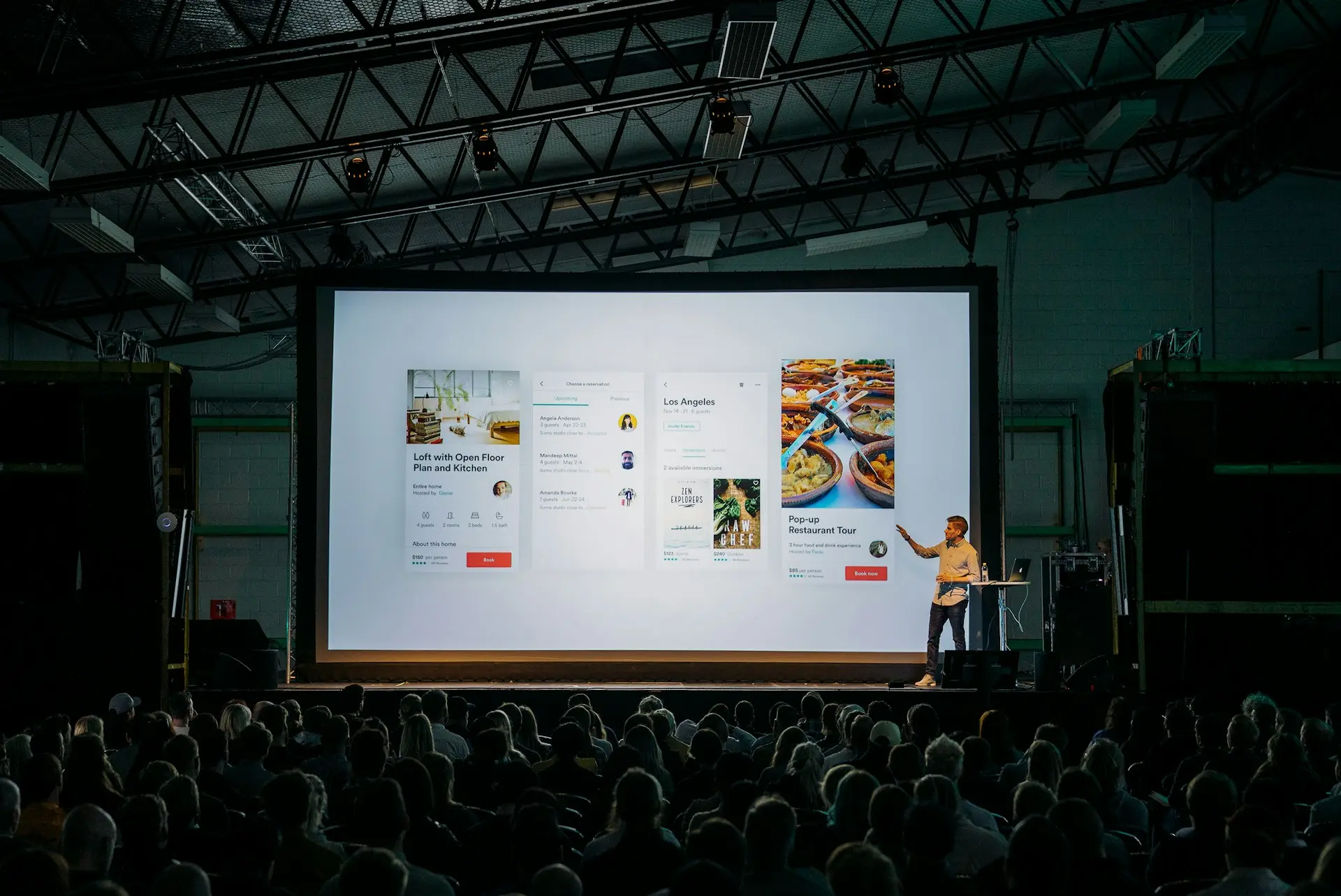 person discussing while standing in front of a large screen in front of people inside dim-lighted room
